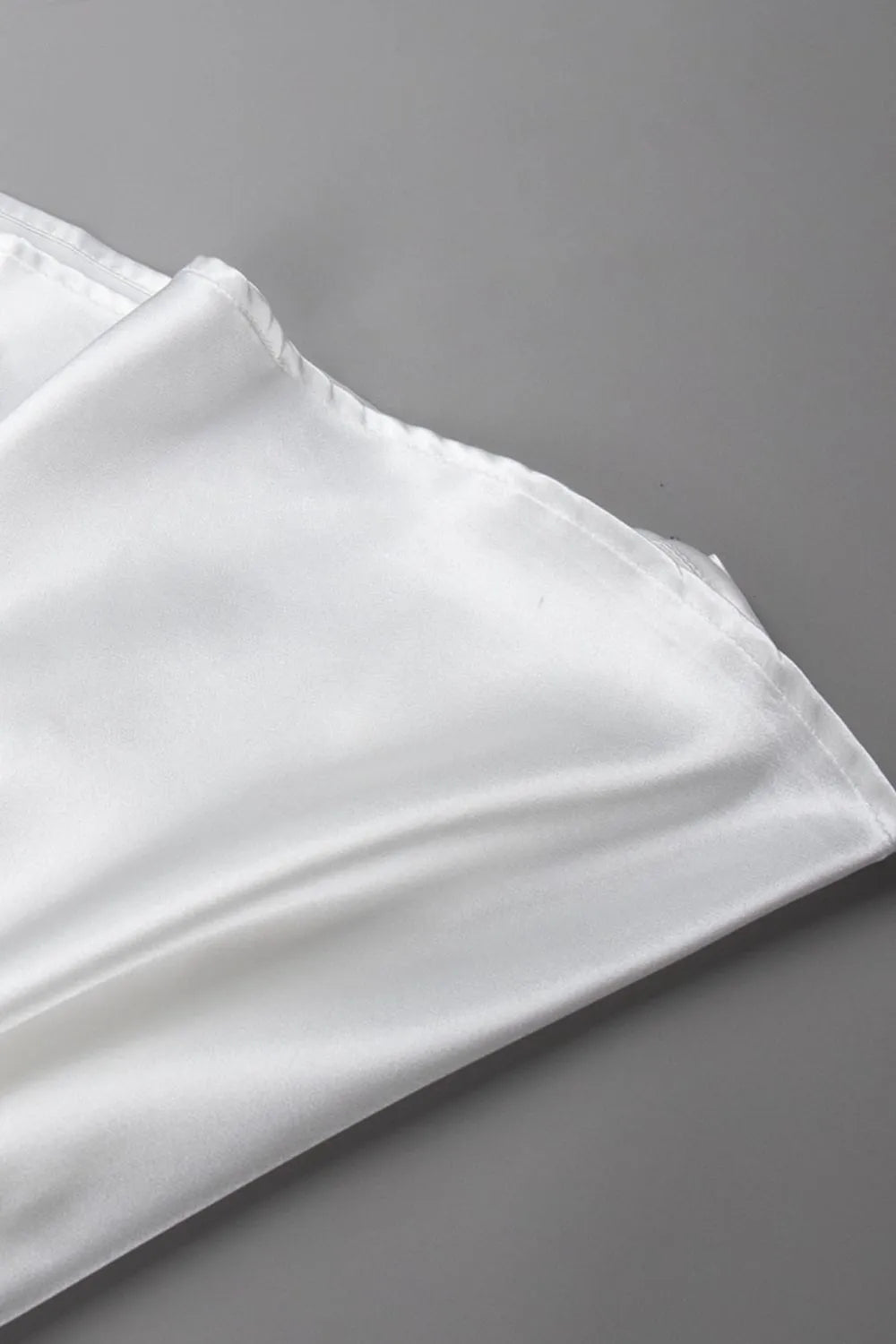 Detail shot of smooth satin fabric and hem of white midi skirt on a grey surface – Voguelle